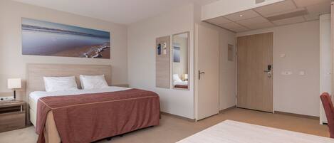 Ein Hotelzimmer mit einem Bett, einem Schreibtisch, einem Stuhl, einem großen Fenster und einer Tür.