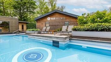 A modern pool area with lounge chairs, a wooden building labeled 'BLUE WELLNESS,' and a clear blue pool.