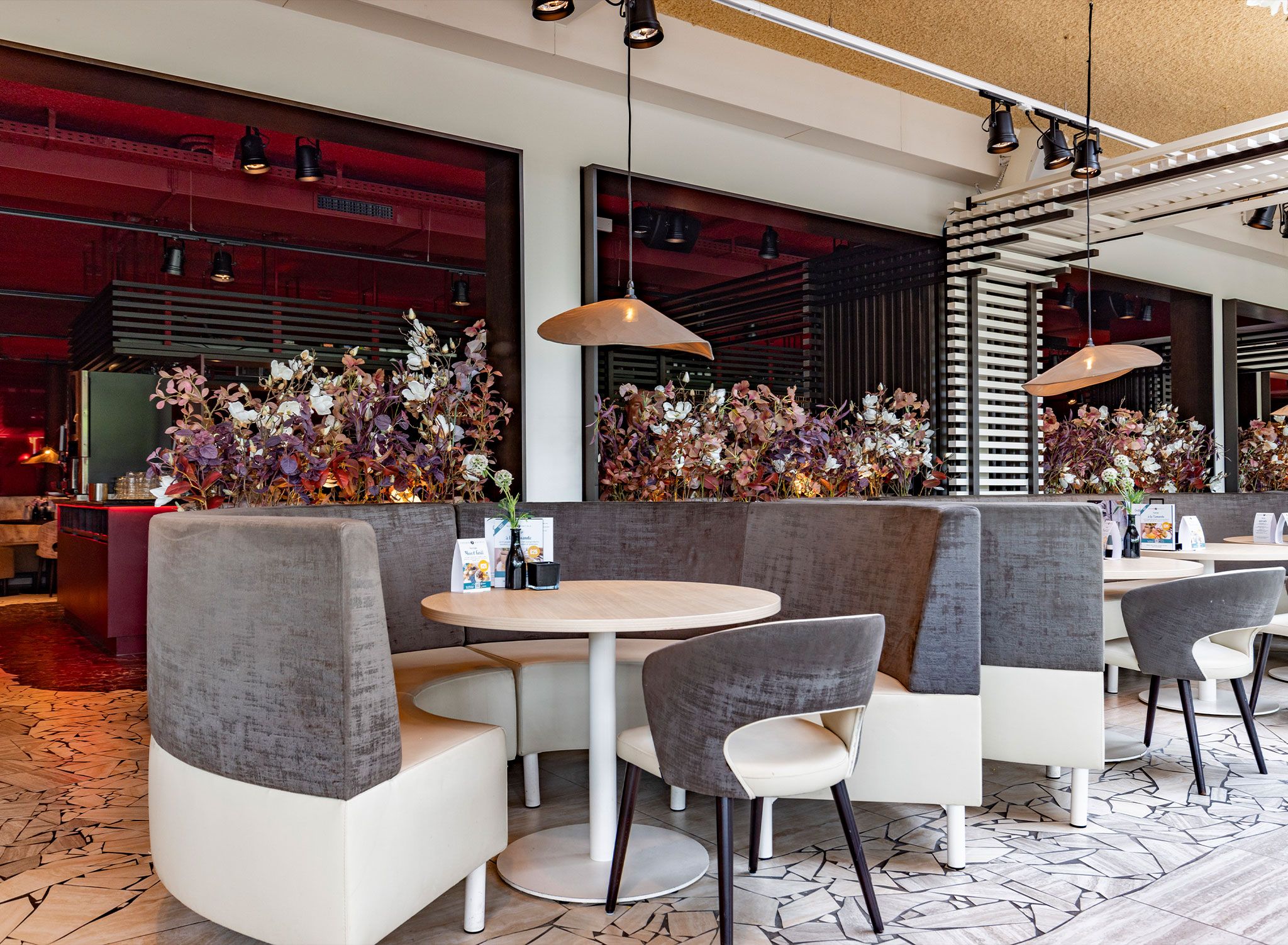 A modern restaurant interior with round tables, cushioned booths, and pendant lighting.