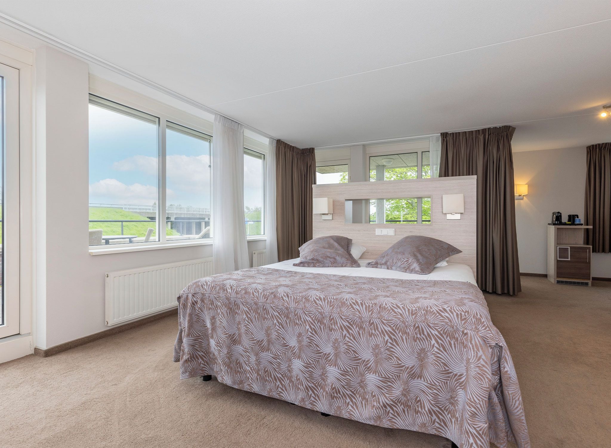 A bedroom with a large bed, a window with a view, a dresser, and a mirror.