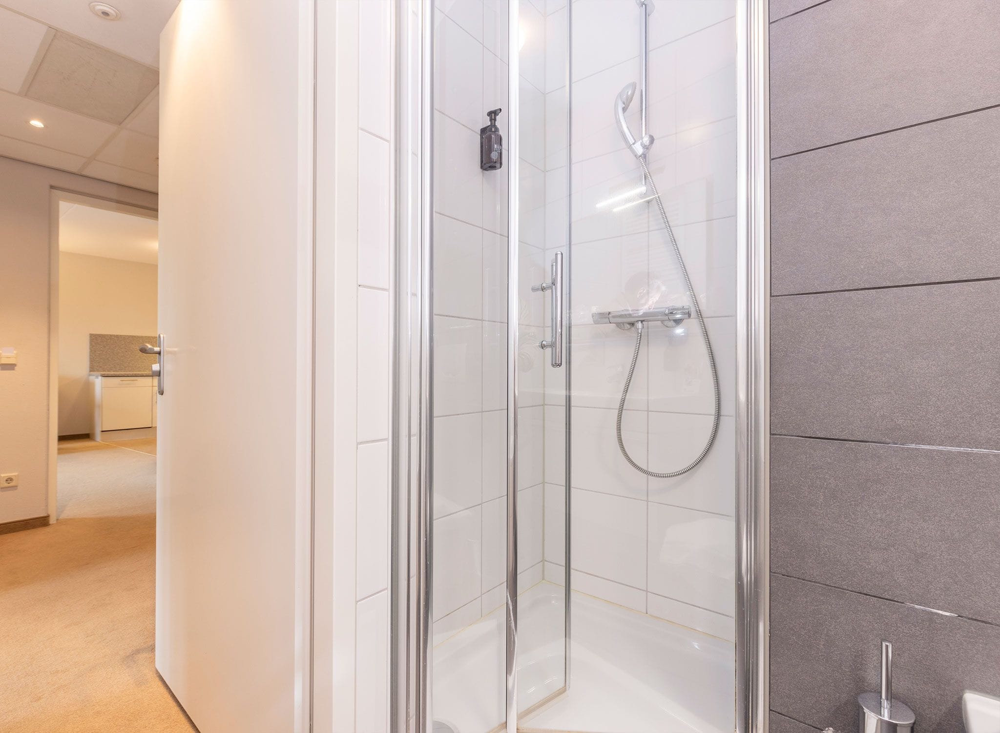 Un baño moderno con ducha de vidrio, cabezal de ducha manual y grifo empotrado.