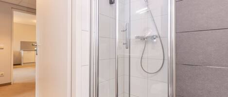 A modern bathroom with a glass-enclosed shower, a handheld showerhead, and a wall-mounted faucet.