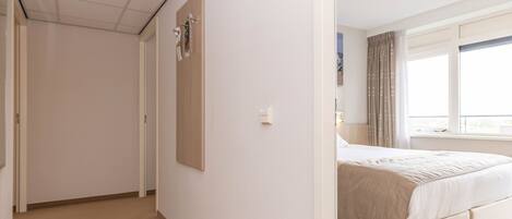 Habitación de hotel con cama, ventana con cortinas, puerta y lámpara fijada a la pared.