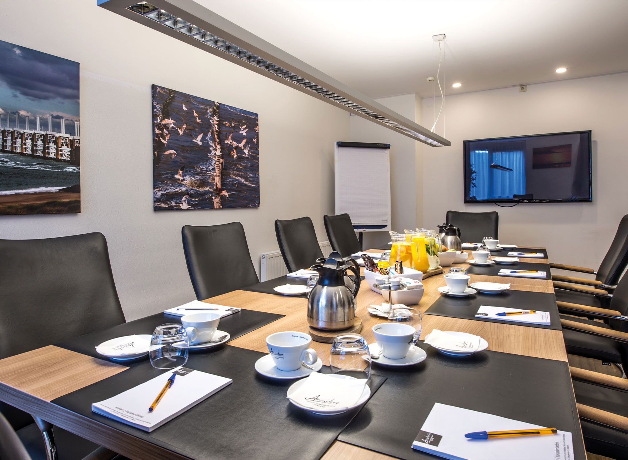 Ein Konferenzraum mit einem langen Tisch, Stühlen, einer Tafel und einem Vogelgemälde an der Wand.