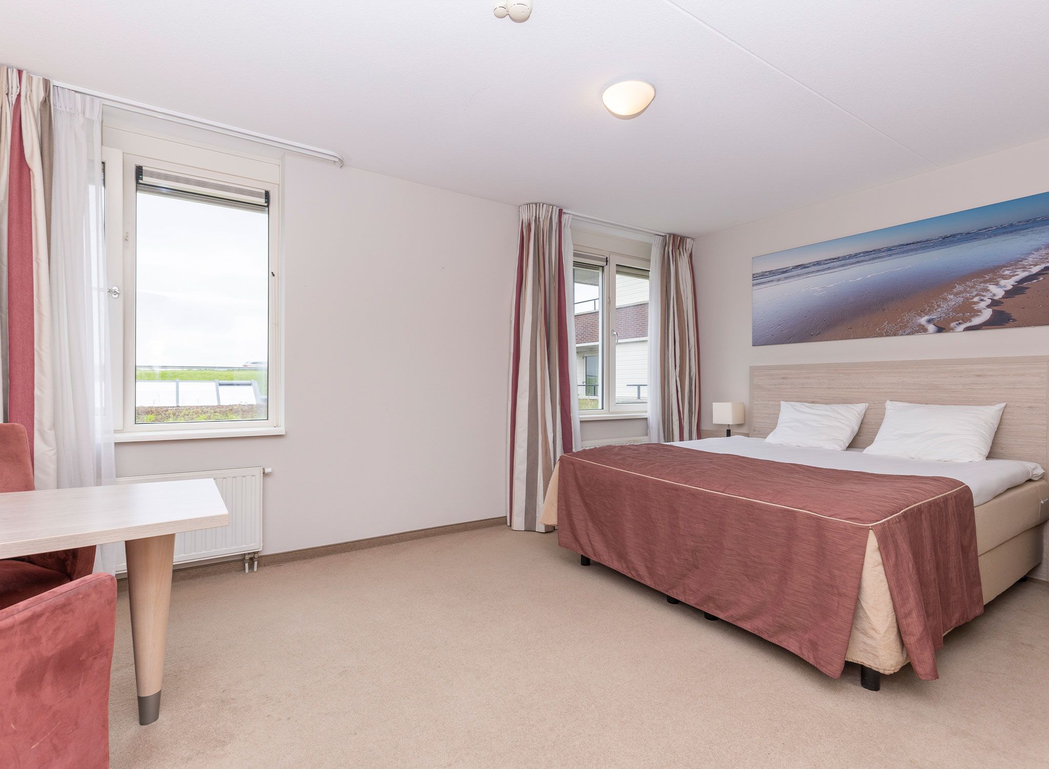 A hotel room with a bed, a desk, and a view of the beach.