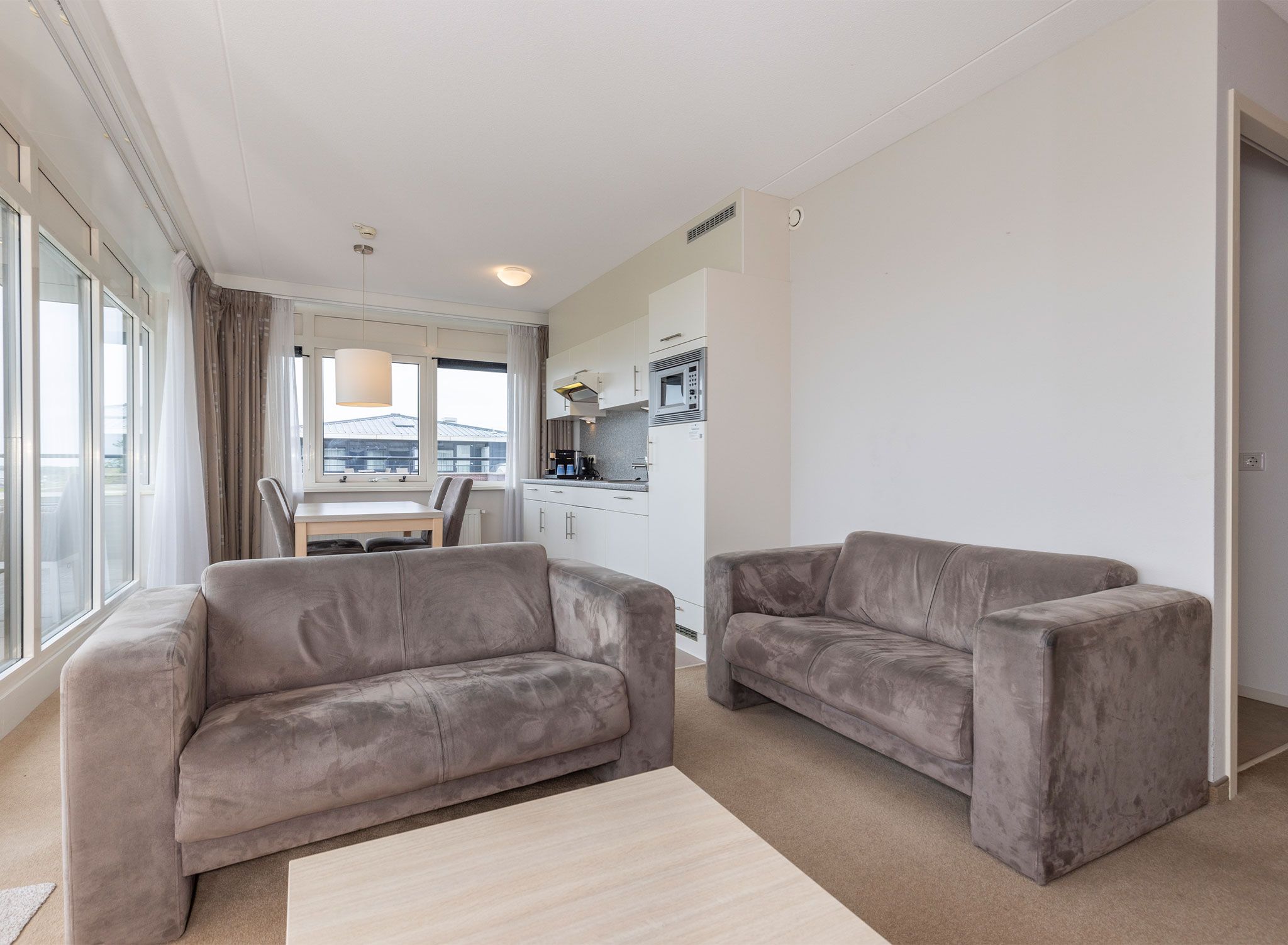 A modern living room with two sofas, a coffee table, and a view of a balcony.