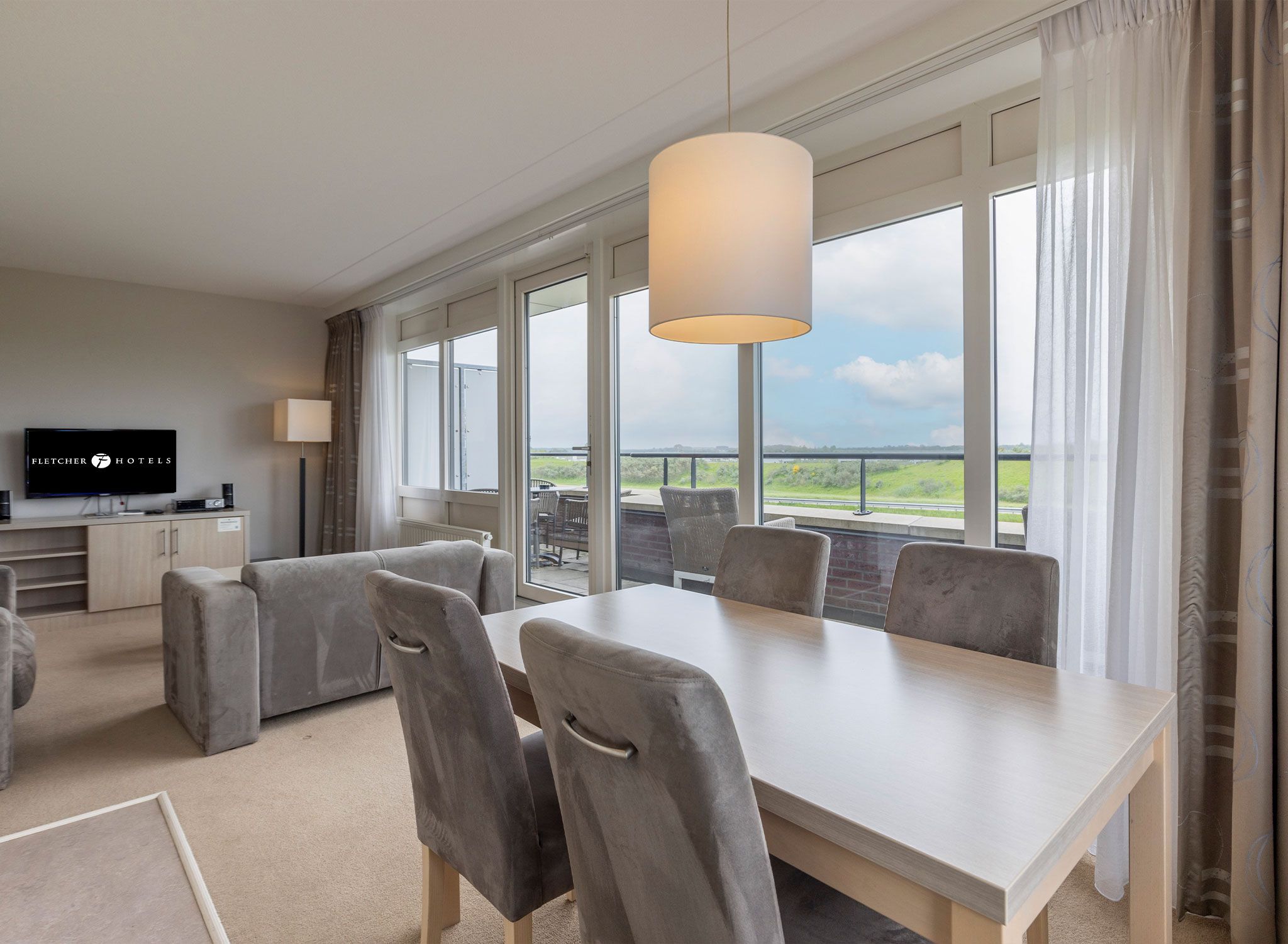 A hotel room with a dining area, a television, and a view of the outdoors.