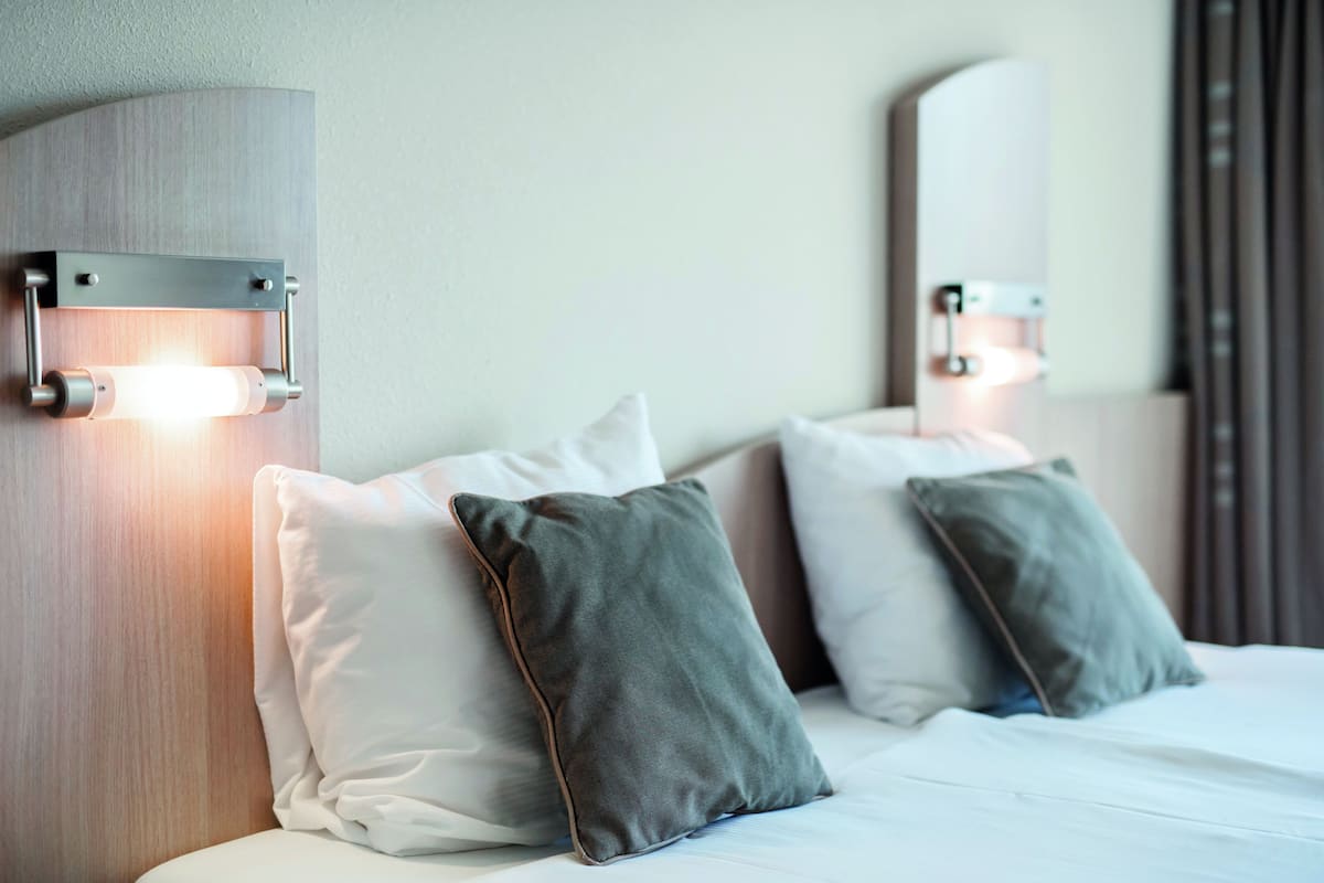 A hotel room with a modern design, featuring a bed with white linens, two pillows, and wall-mounted lighting fixtures.