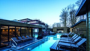 A swimming pool with lounge chairs and a wooden deck, surrounded by buildings and trees.