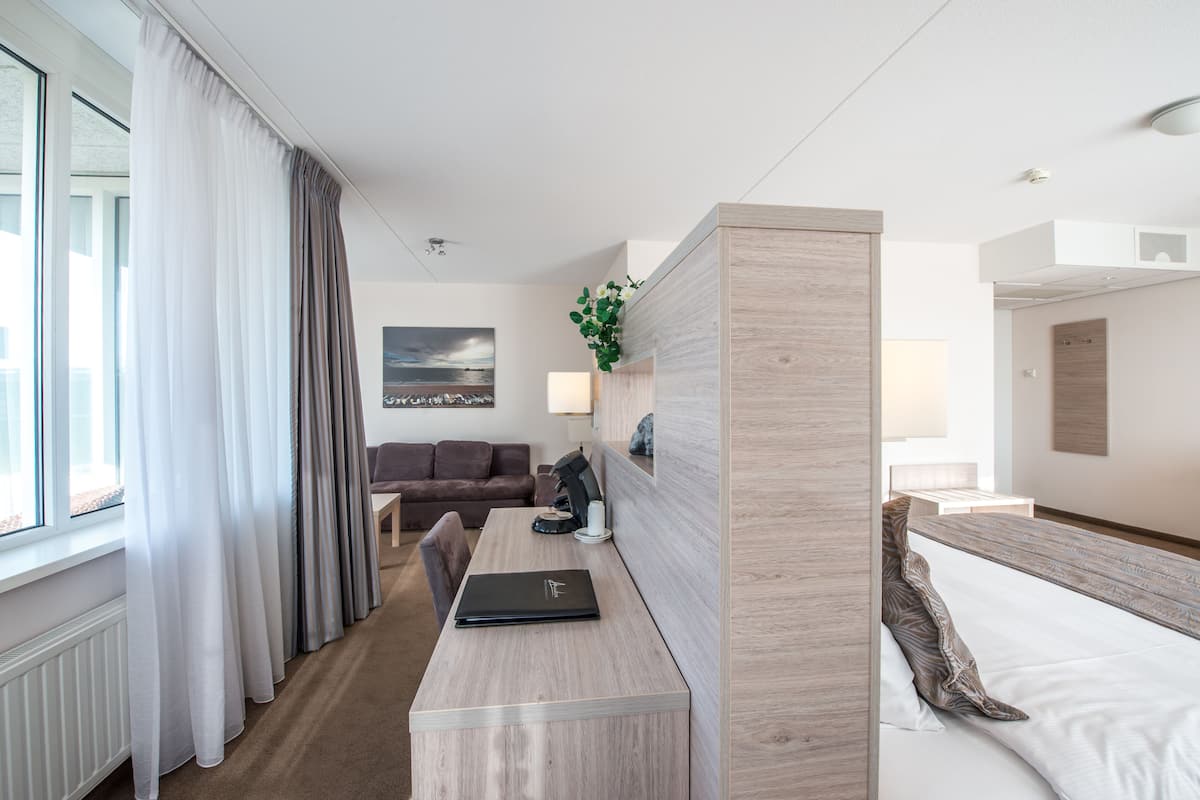 A hotel room with a bed, a desk with a laptop, a sofa, and a view of the city.