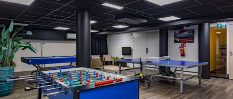 Een kamer met een tafelvoetbaltafel, een pingpongtafel en een televisie.