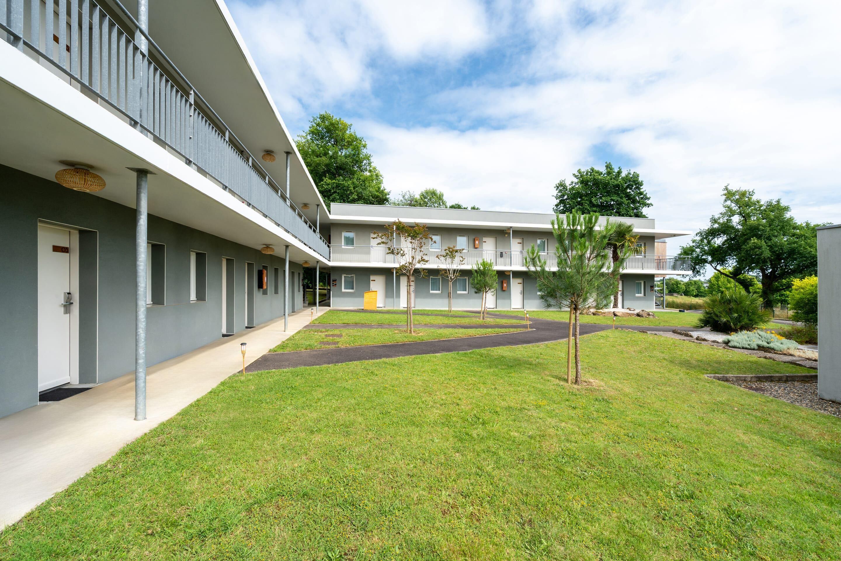 A modern building with a flat roof, a covered walkway, and a well-maintained lawn with young trees.
