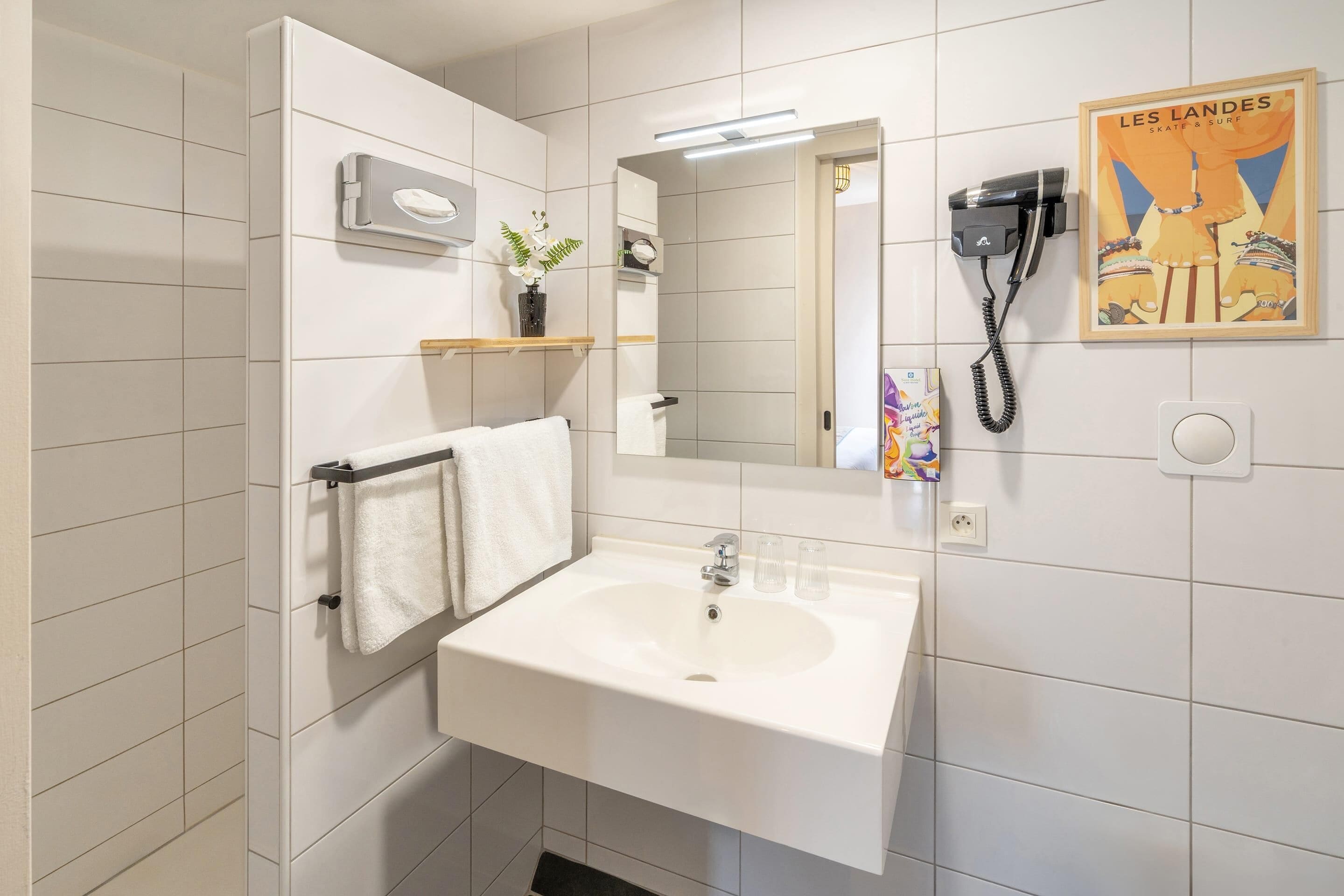 A bathroom with a white sink, a mirror, a hairdryer, and a poster on the wall.