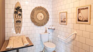 A bathroom with a toilet, a sink, a mirror, and a surfboard decoration.