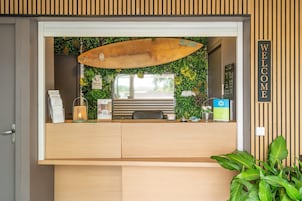 Un mostrador de recepción con una decoración de tabla de surf, un cartel que dice 'WELCOME' y una pared verde con plantas.