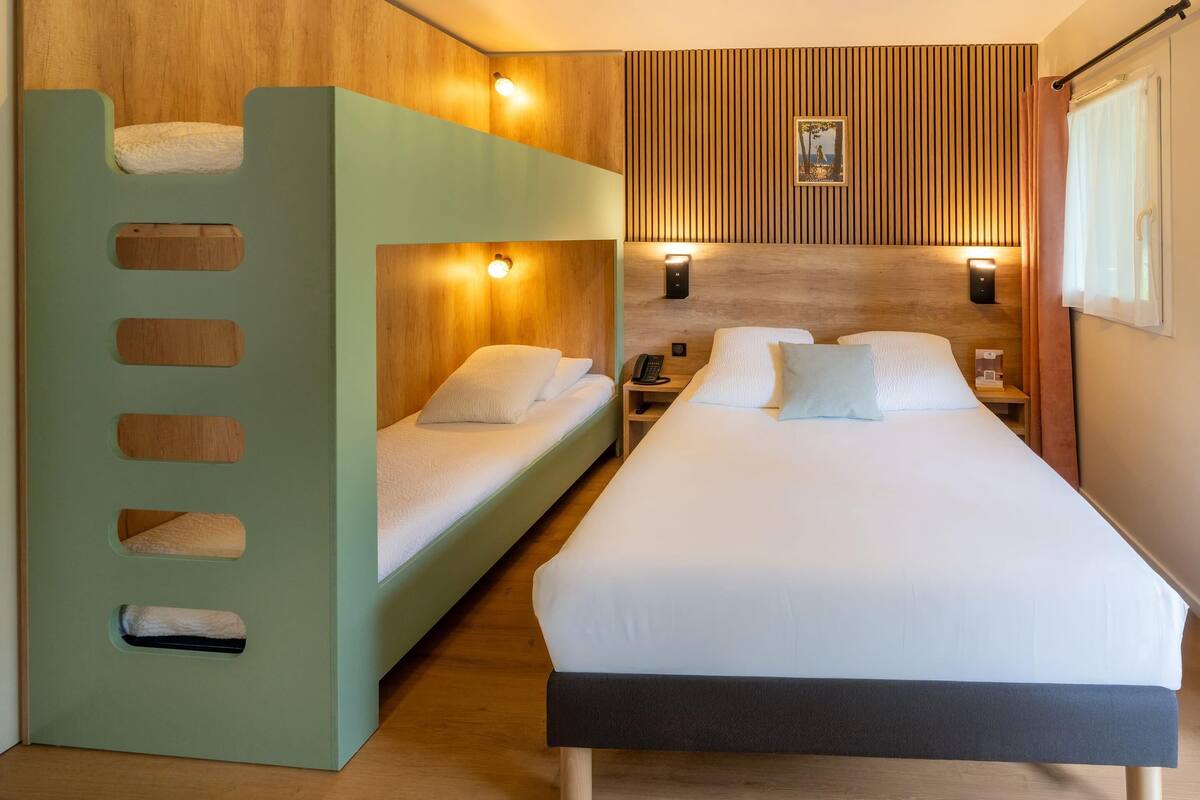 A hotel room with bunk beds, a wooden headboard, bedside lamps, and a framed picture on the wall.