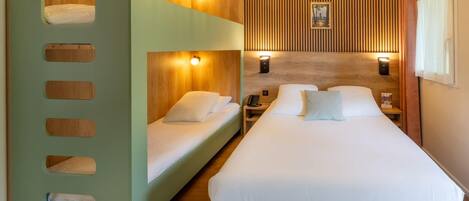 Habitación de hotel con literas, cabecera de madera, lámparas de noche y un cuadro en la pared.
