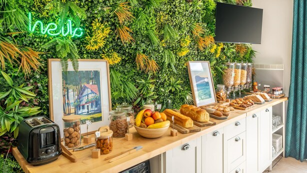 Una barra de desayuno con diversas opciones de comida, un tostador y una pared decorada con plantas y un letrero de neón.