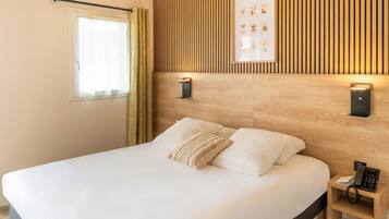 A hotel room with a large bed, a wooden headboard, a bedside table with a phone, and a window with curtains.