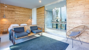 A modern room with a wooden wall, a sofa, a chair, and a dining area visible through a glass door.
