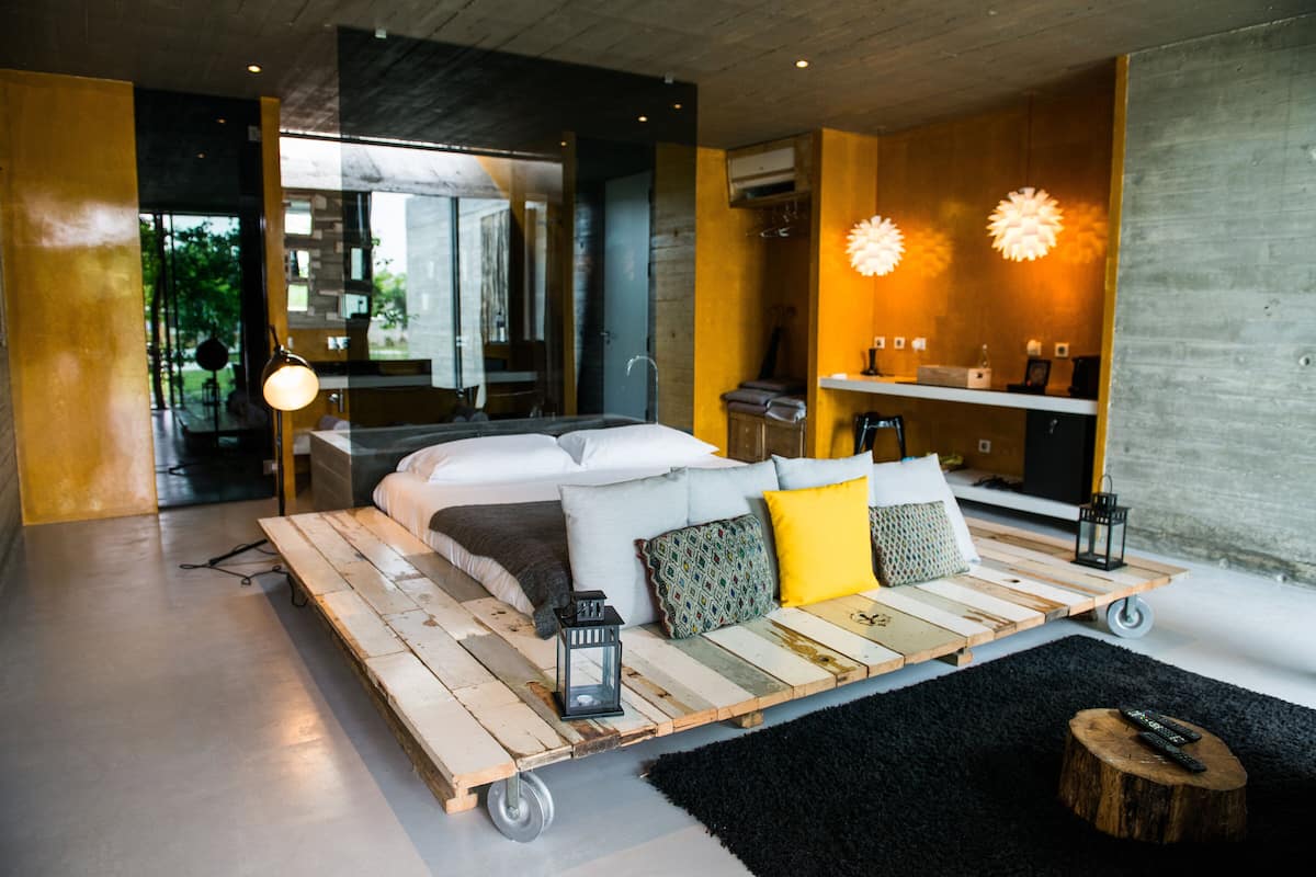Ein modernes Schlafzimmer mit einem Bett auf einer Holzplattform, einem schwarzen Teppich und einem kleinen Holzschemel.