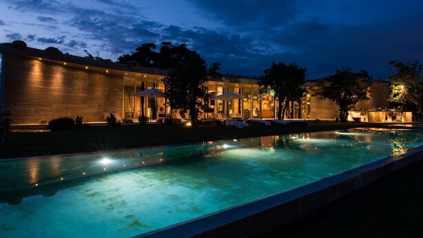A modern hotel with a swimming pool, outdoor seating, and a well-lit facade.