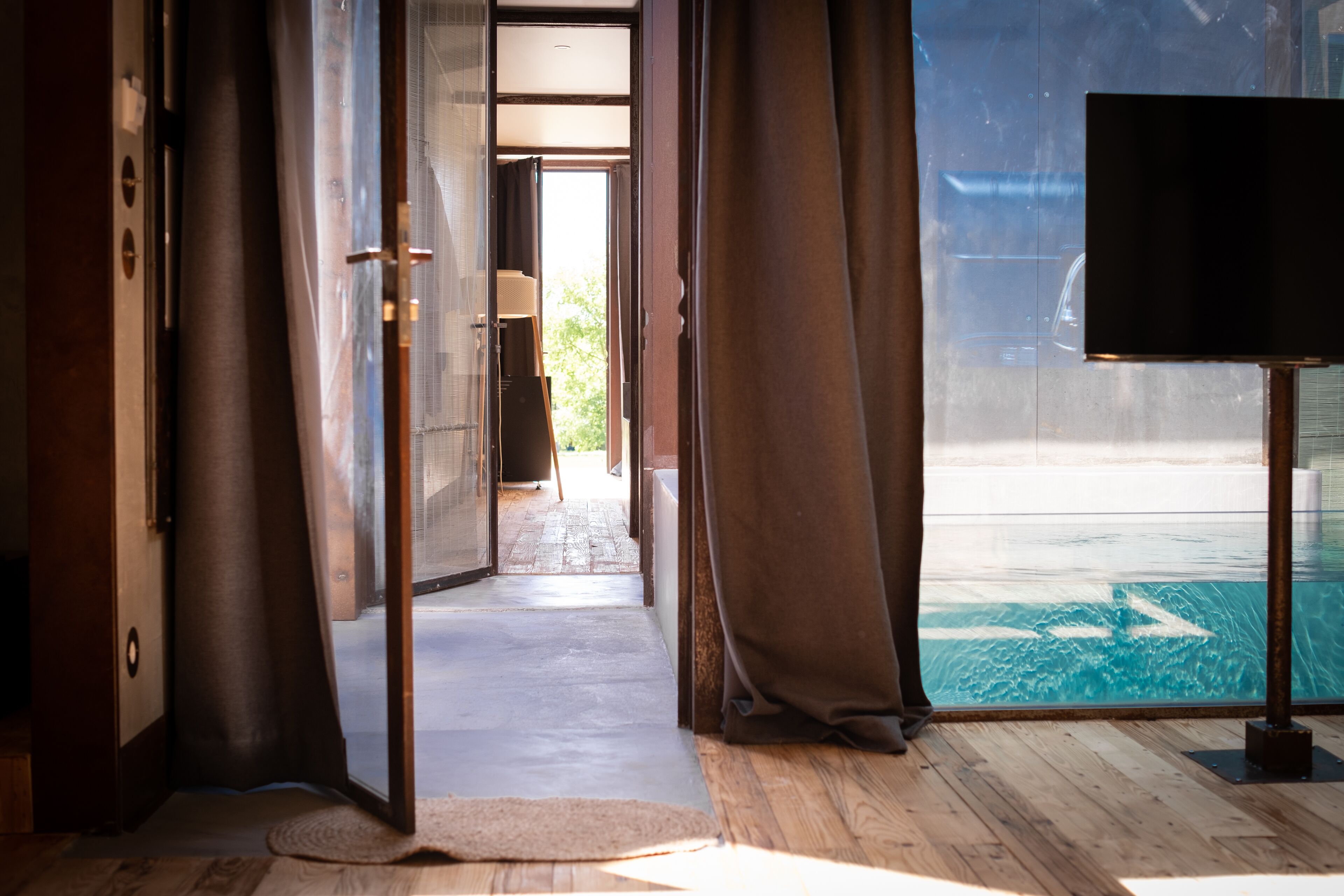 An open doorway leading to a wooden deck with a pool, curtains on either side, and a television on the right.