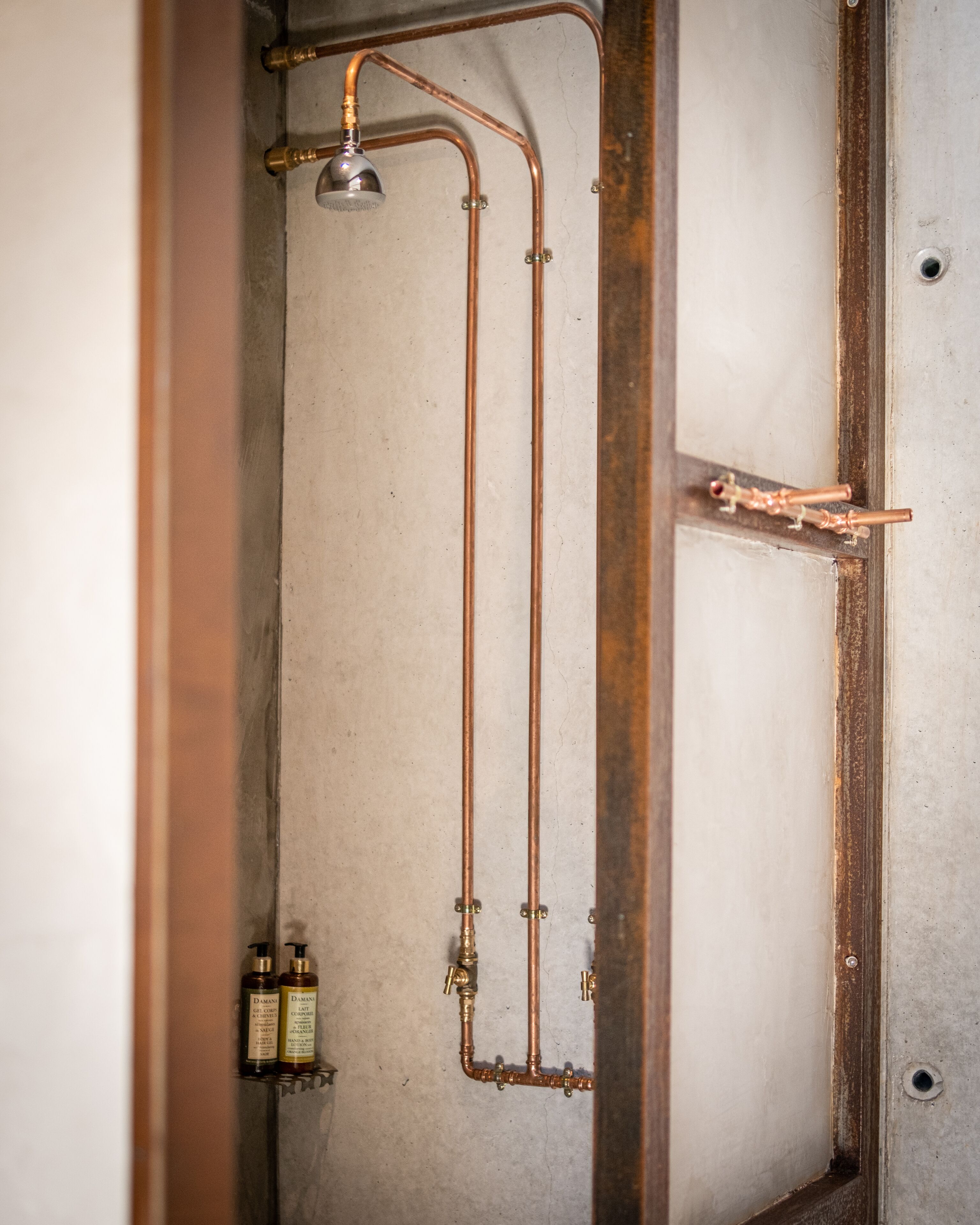 Un baño con cañerías de cobre, un cabezal de ducha y dos botellas de champú.