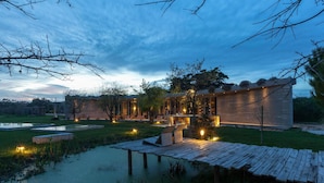 A modern outdoor setting with a wooden deck, a small pond, and a building with large windows and a flat roof.