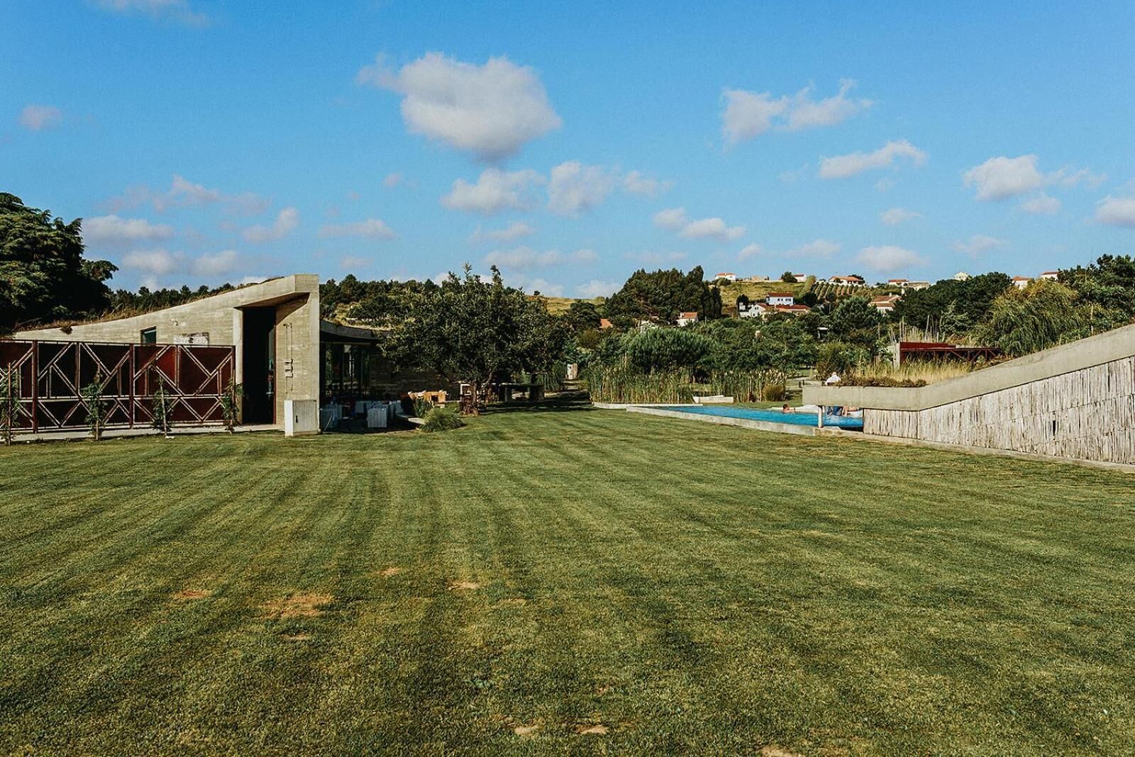 Un espacio verde cuidado con una piscina, una estructura de concreto y vistas a una colina con casas.