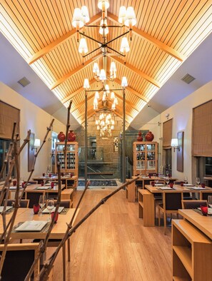 Un restaurante con mesas de madera, un techo alto con diseño de listones de madera y una lámpara central.