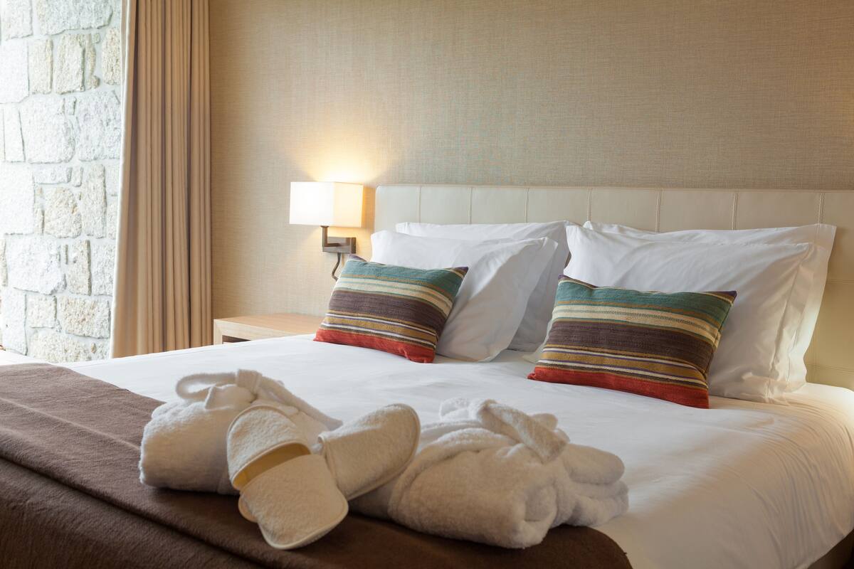 A neatly made bed with white linens, two striped pillows, and a brown throw blanket.