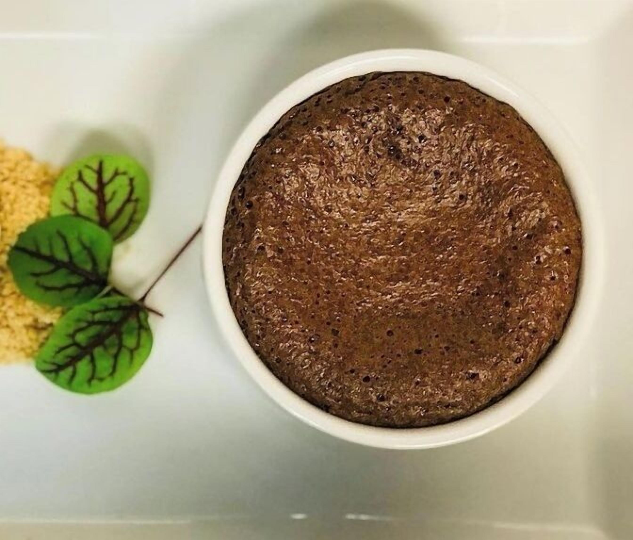 Un bol blanc contenant un gâteau brun foncé, posé sur une surface blanche.