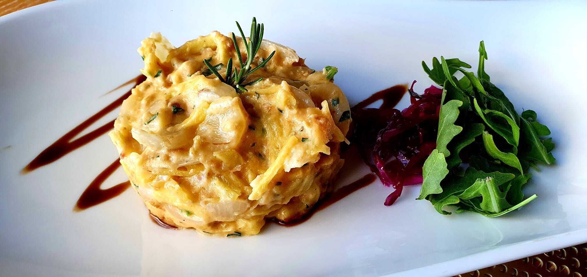 A dish with a creamy texture, garnished with a sprig of rosemary, and accompanied by a side of red cabbage and green leaves.
