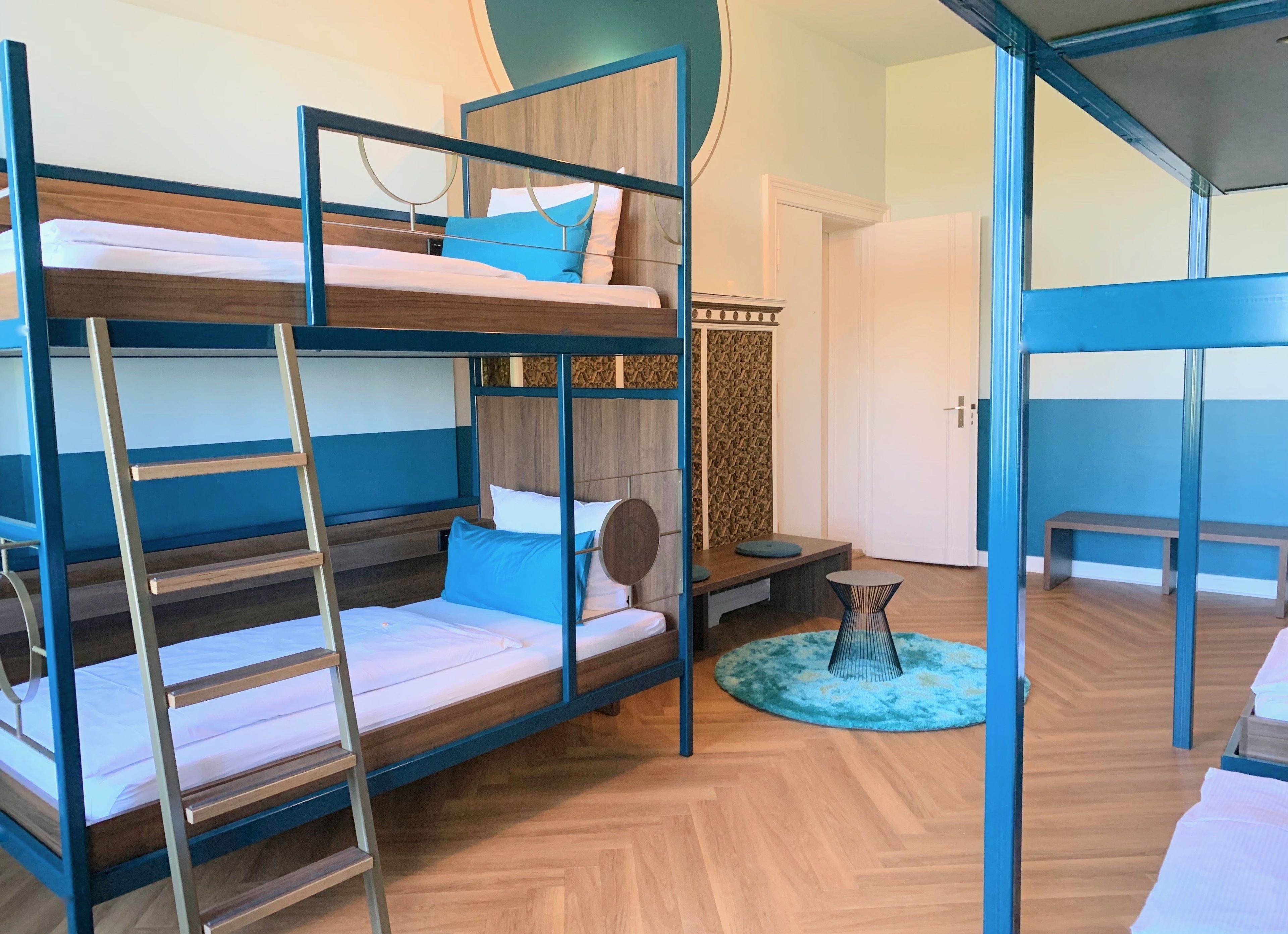 A bunk bed room with a wooden floor, a small round table, and a bench.