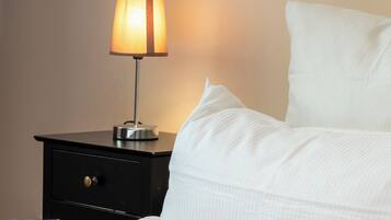 A neatly made bed with white bedding, a bedside lamp, and a small black nightstand with a drawer.