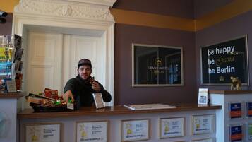 Un comptoir d’accueil orné de trophées encadrés, une enseigne sur laquelle on peut lire « Soyez heureux, soyez Grand Berlin », et une photo encadrée de l’hôtel.
