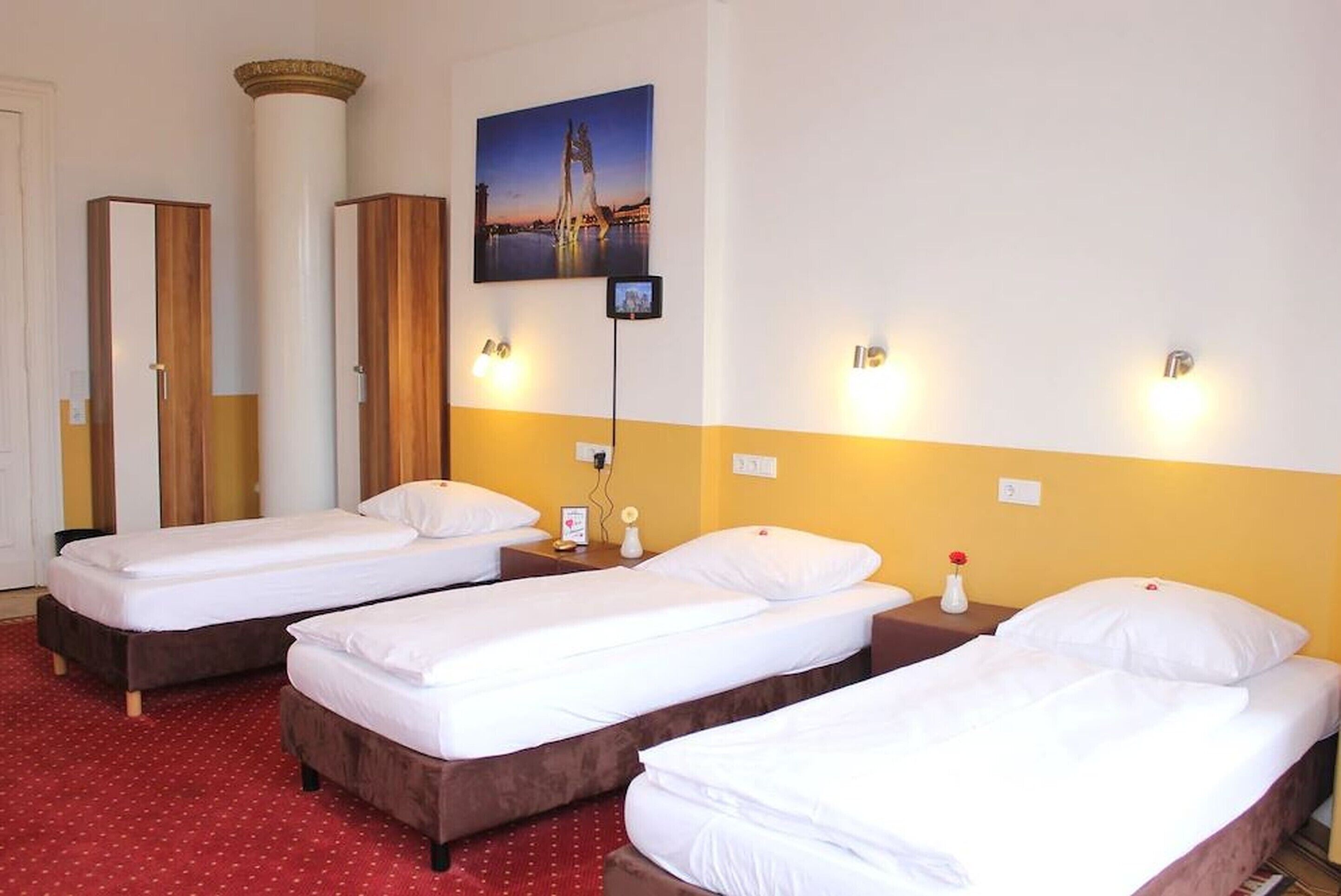 Una habitación de hotel con tres camas individuales, un ventanal grande y un cuadro de un puente.