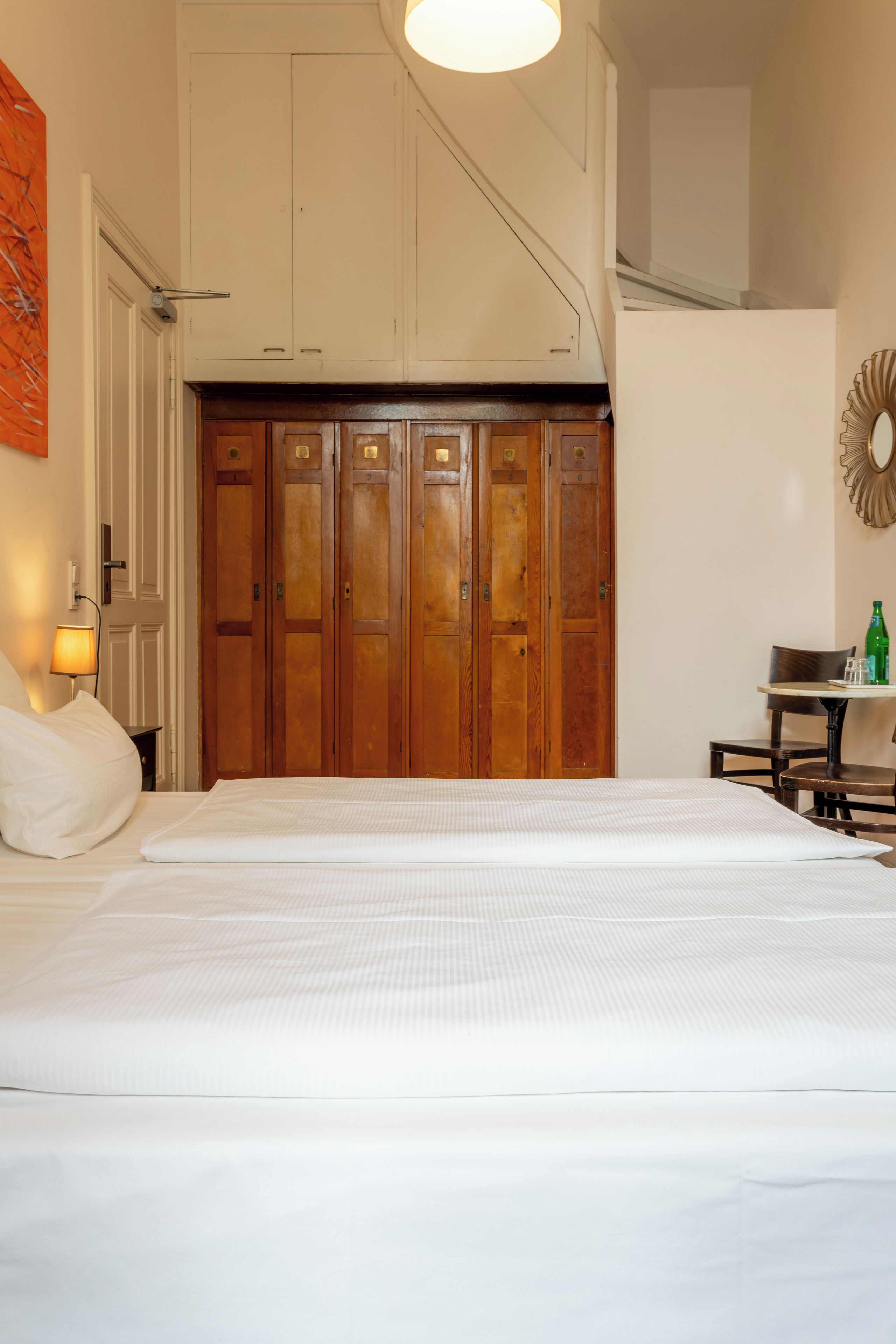 A bedroom with a large bed, wooden wardrobe, and a small table with a bottle.