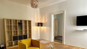 A living room with a yellow armchair, a white table, a floor lamp, a bookshelf, and a TV on the wall. - Grand Hostel Berlin Classic (Berlin)