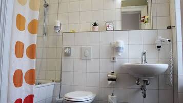 A bathroom with a toilet, sink, shower, and a mirror.