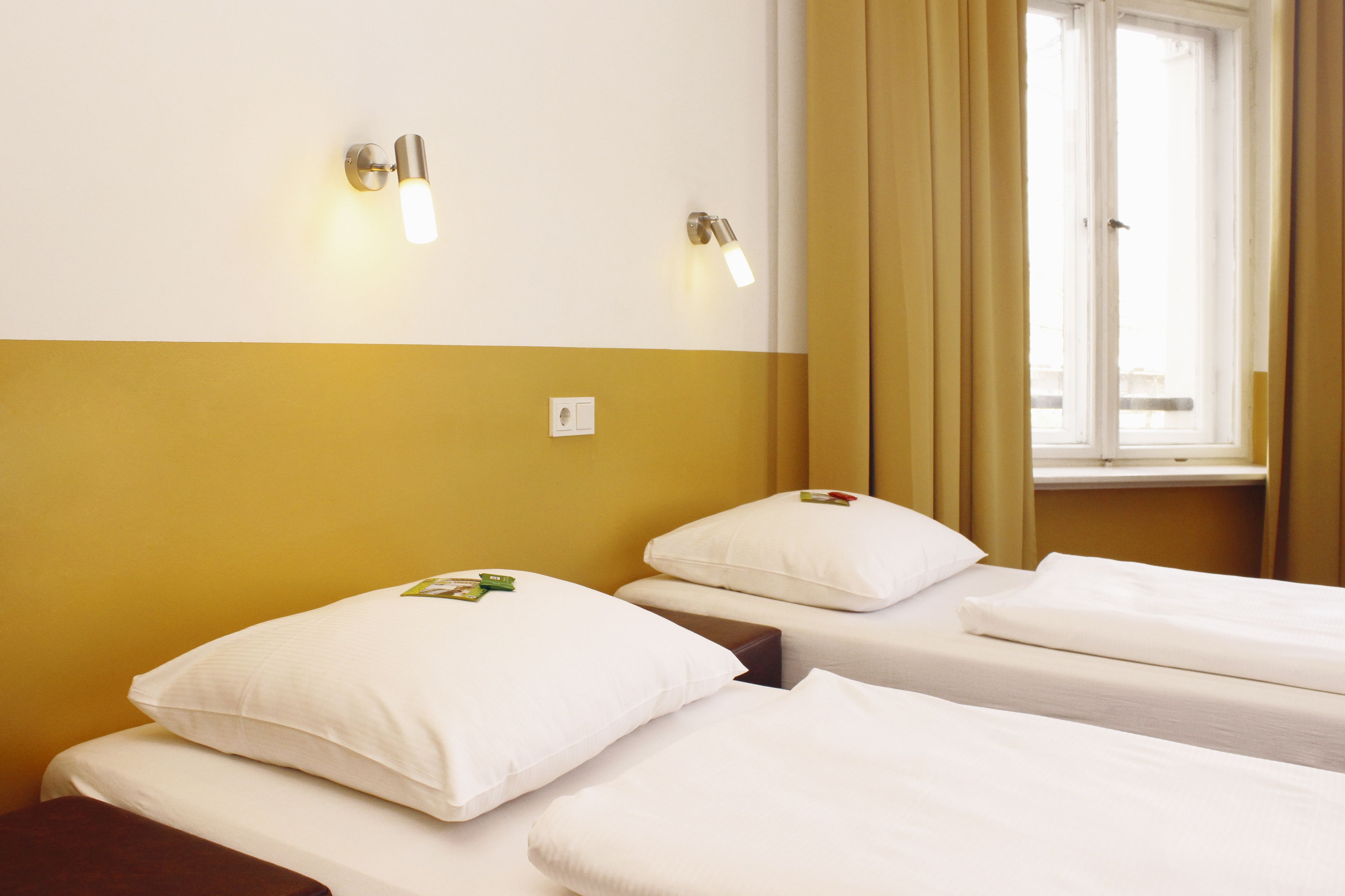 Ein Hotelzimmer mit zwei Einzelbetten, einem Fenster mit Vorhängen und Wandleuchten.