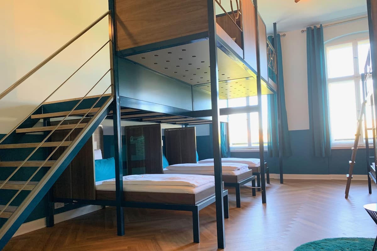 A dormitory-style room with bunk beds, a staircase, and a view of the outside through a window.