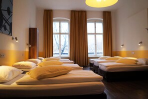 A hotel room with multiple beds arranged in a row, large windows with curtains, and wall-mounted lights. - Grand Hostel Berlin Classic (Berlin)