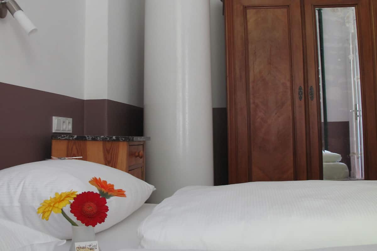 A hotel room with a bed, a wooden wardrobe, a white pillar, and a wall-mounted light fixture.