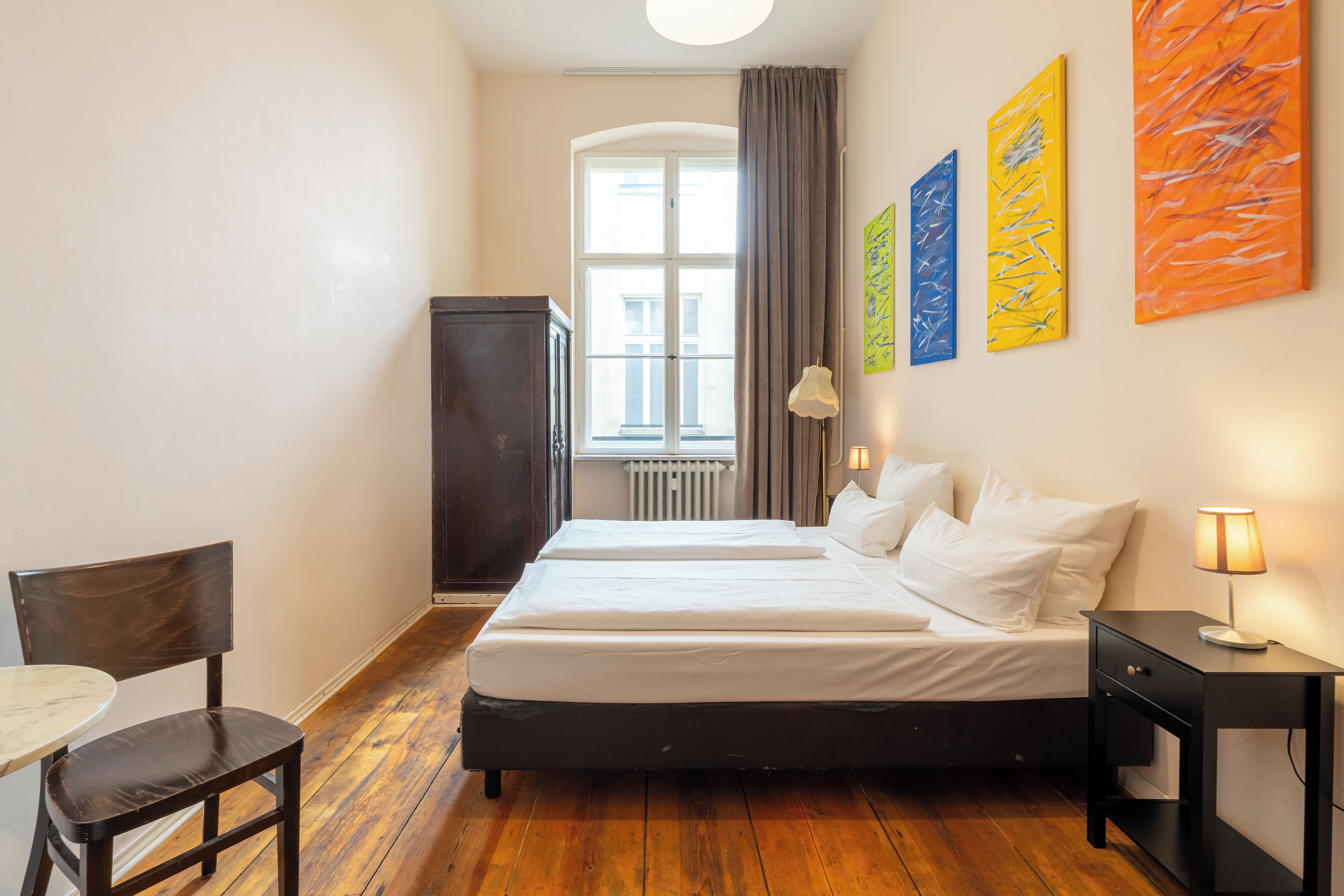 Una habitación de hotel con una cama, un escritorio, una silla y un ventanal con cortinas.