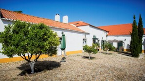 Ein Innenhof mit Kopfsteinpflaster, weißen Gebäuden mit orangenen Akzenten und grünen Bäumen.