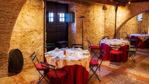 Ein rustikaler Essbereich mit Steinwänden und Gewölbedecken, mit runden Tischen mit roten Tischdecken und Stühlen.