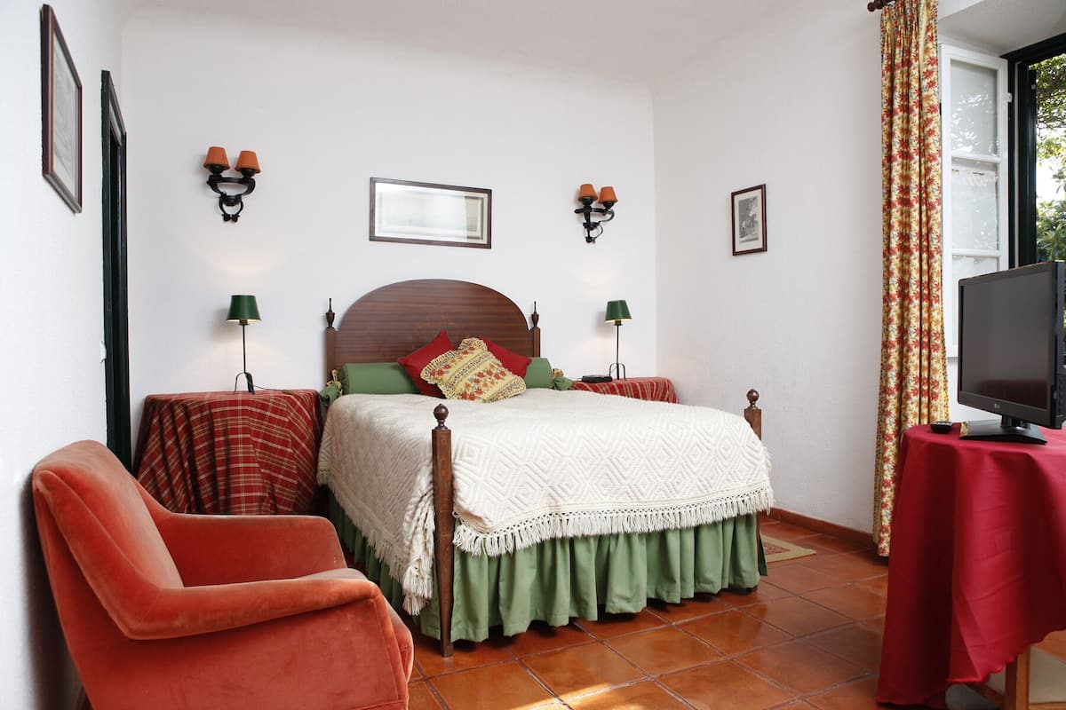 A bedroom with a bed, two bedside tables, a chair, a TV, and a window with curtains.