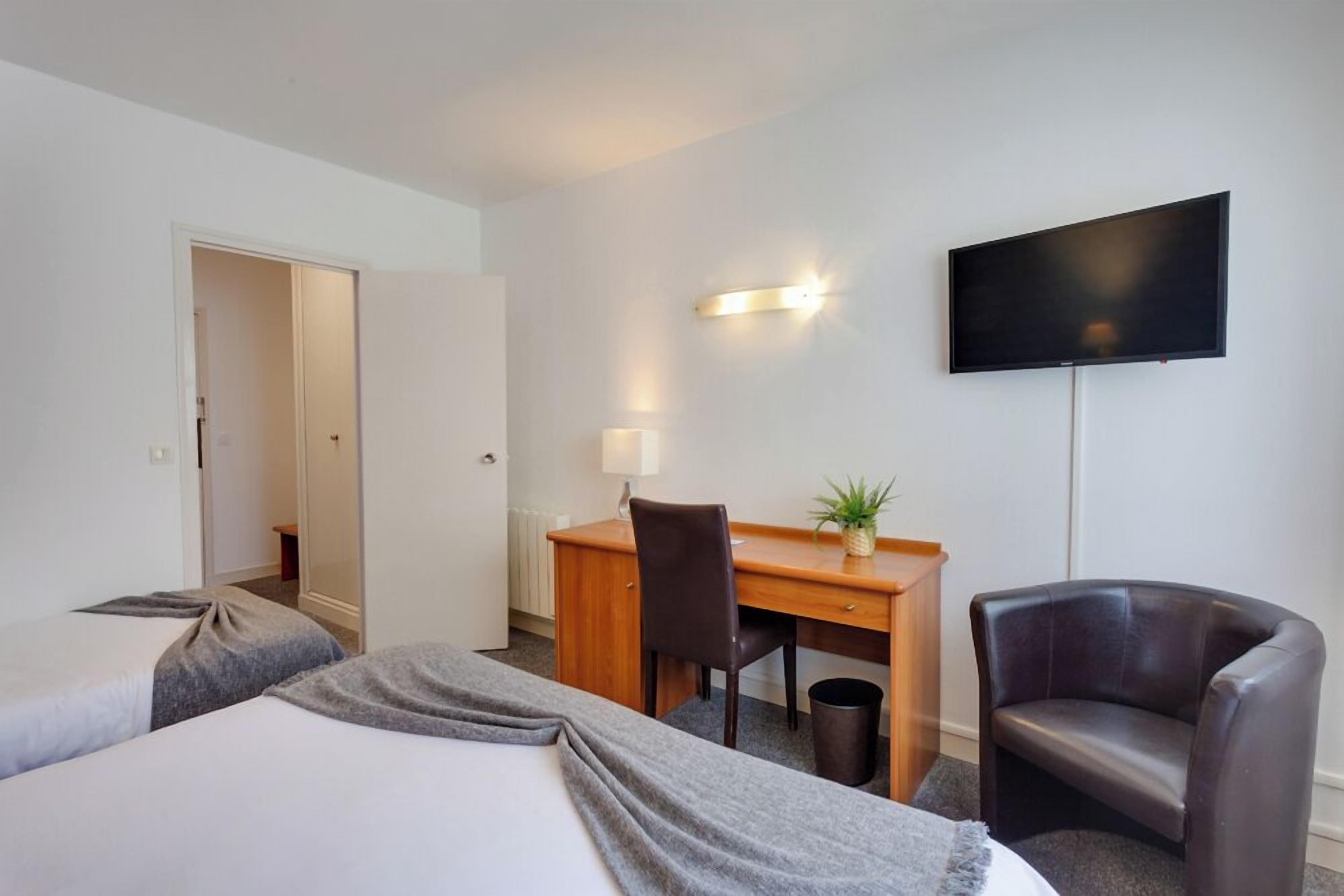 Une chambre d’hôtel avec deux lits, un bureau, une chaise, une télévision et une petite plante.